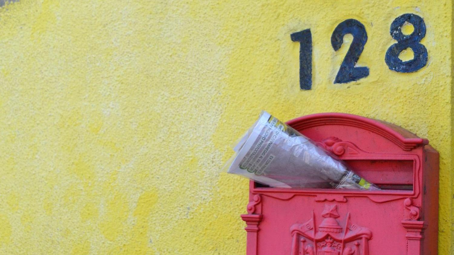Zeitschrift steckt in einem roten, südeuropäisch anmutenden Briefkasten an gelber Hauswand