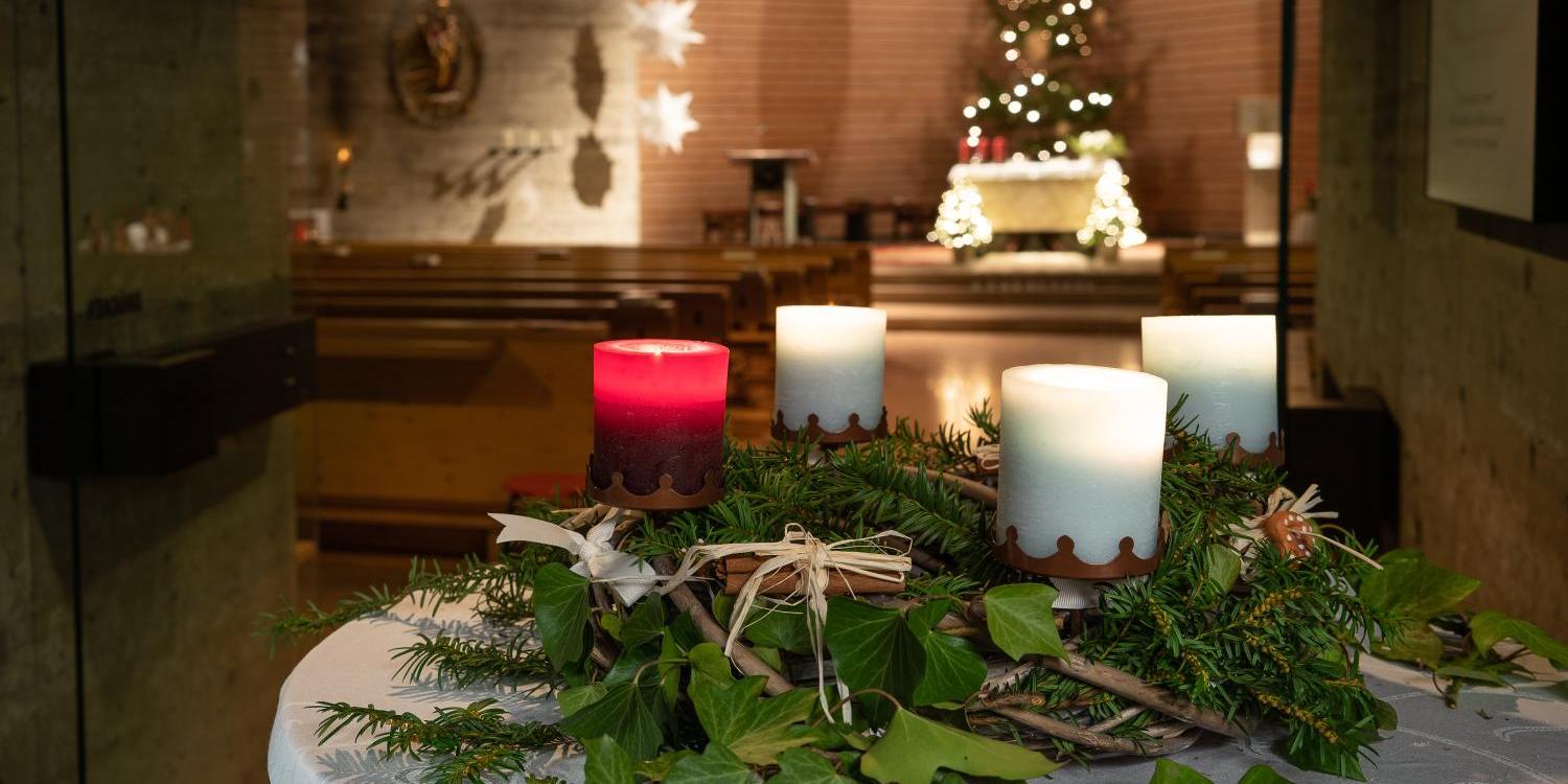 Blick in eine Kirche zu Weihnachten, im Vordergrund ein Adventskranz, im Hintergrund der geschmückte Chor