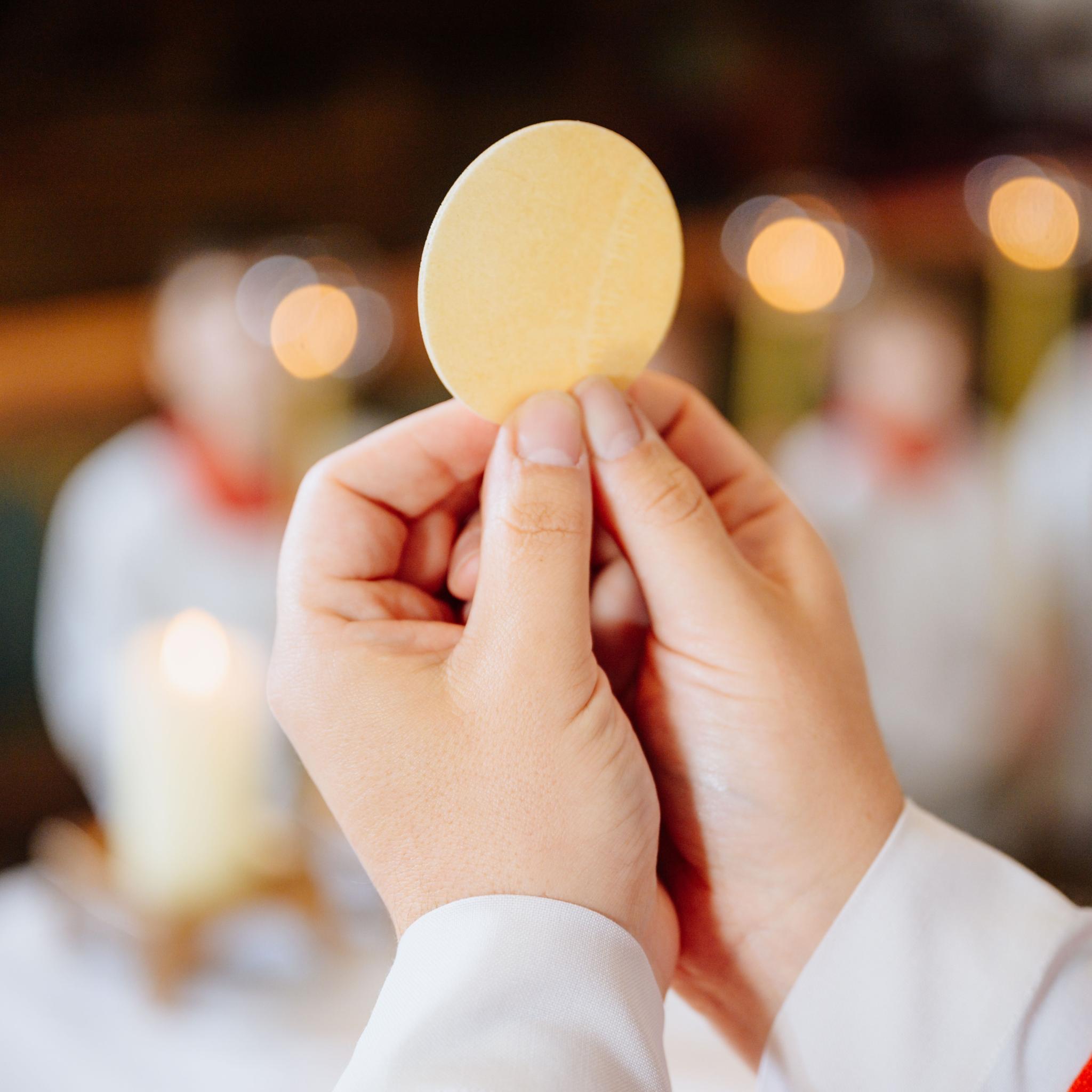 Ein Priester hält eine Hostie während der Eucharistiefeier hoch